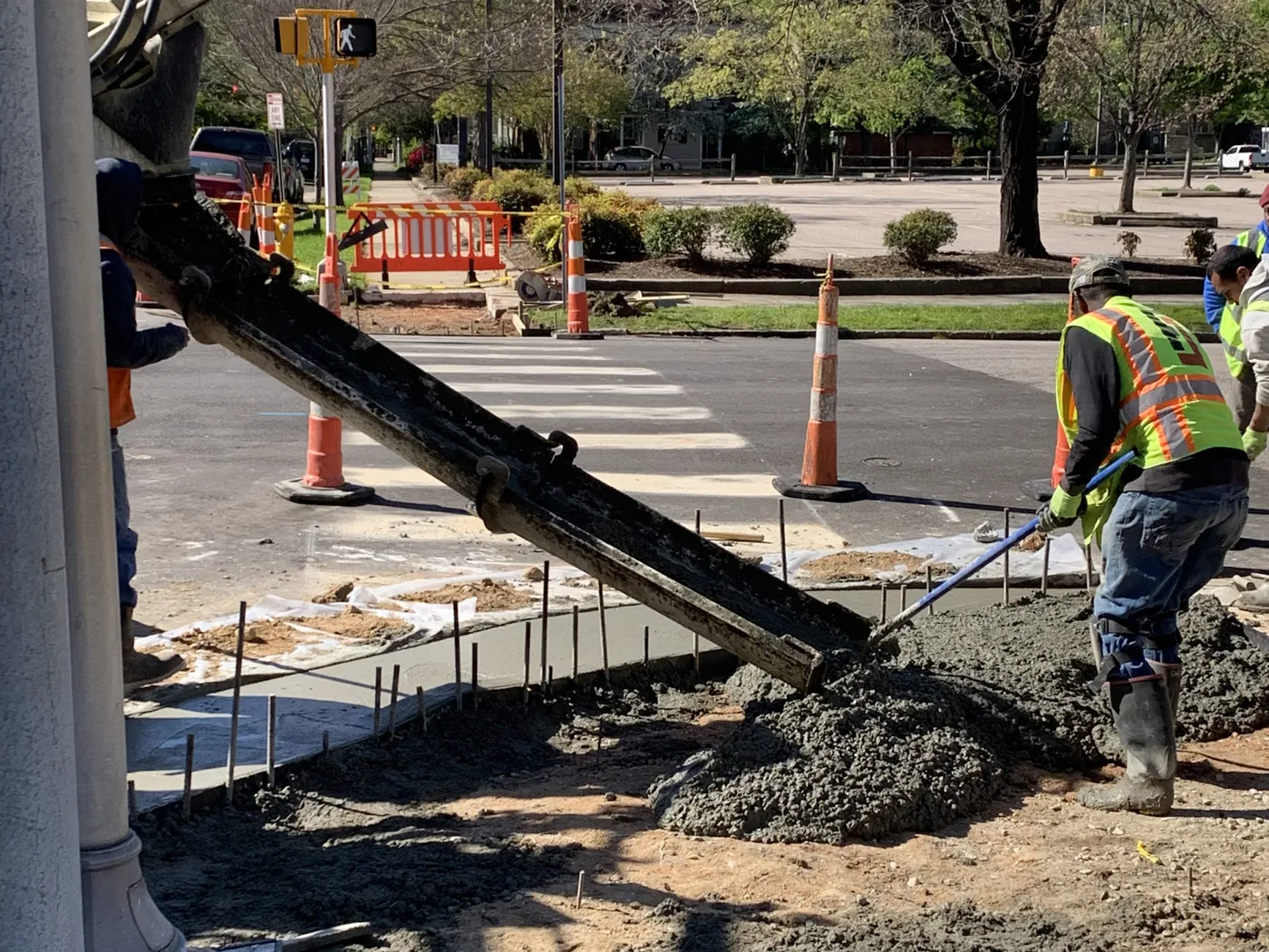 Commercial concrete sidewalk section being placed from a concrete truck chute beside a parking lot, traffic cones set out